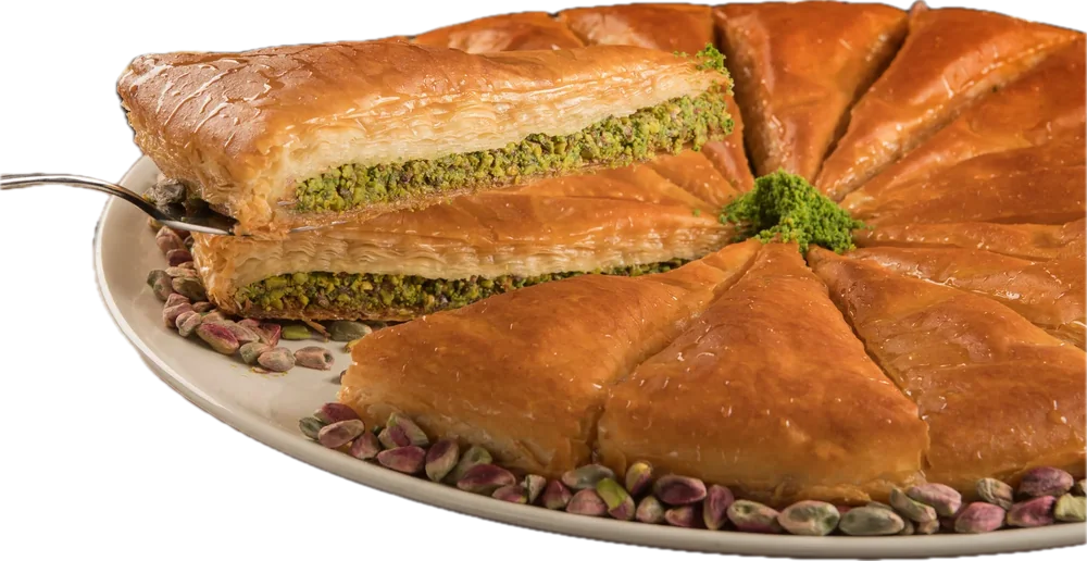A round pistachio baklava cut into wedges on a plate, whole pistachios scattered around it.