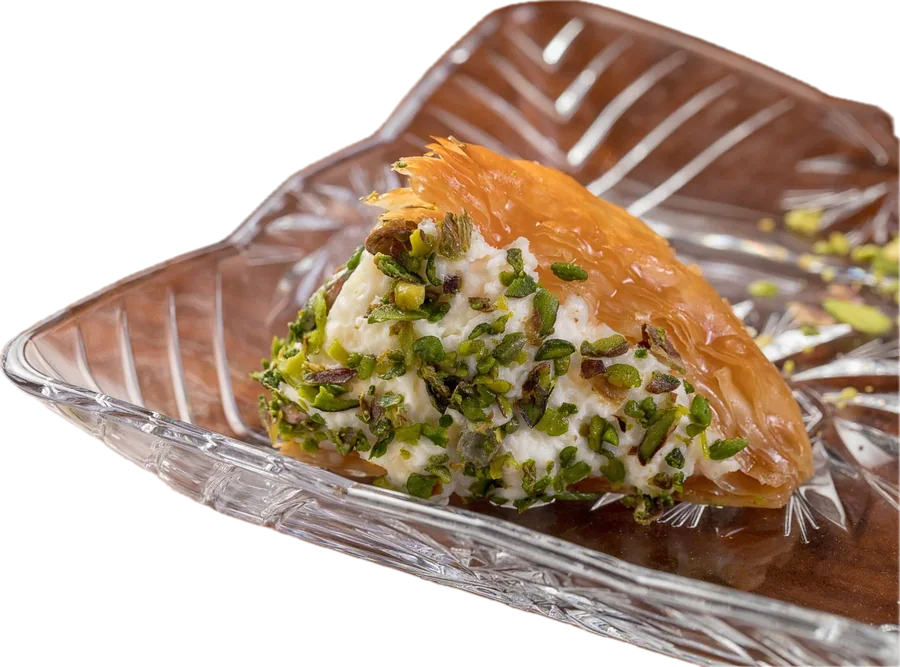 A single warbat pastry filled with clotted cream and crowned with chopped pistachio, on a cut-glass plate.